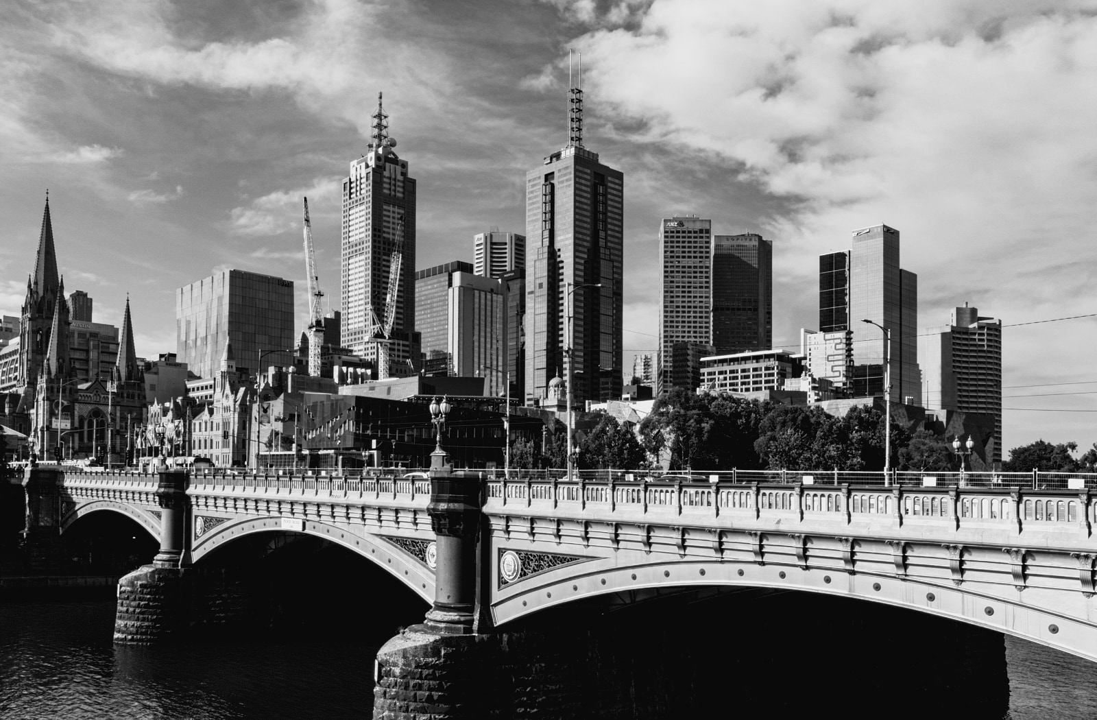 The Melbourne city skyline behind Princes Bridge over the Yarra River, in black and white.